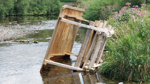 Eine Sitzgelegenheit aus Holz liegt im Fluss.