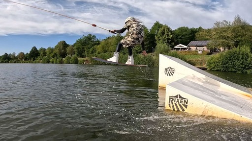 Junge der mit einem Wakeboard über eine Schanze auf einem See springt