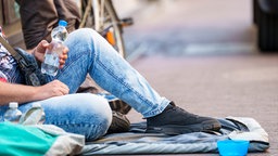 Ein Obdachloser sitzt auf dem Boden mit einer Flasche Wasser in der Hand.