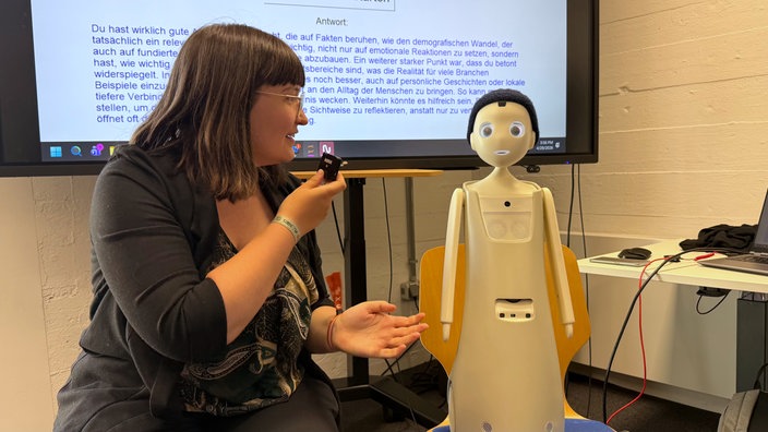 Eine Frau spricht zu einem kleinen Roboter, der auf einem Stuhl steht
