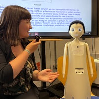 Eine Frau spricht zu einem kleinen Roboter, der auf einem Stuhl steht