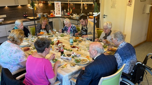 Mehrere Menschen sitzen um herbstlich dekorierten Tisch und essen