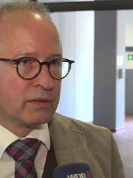 Der Rechtsanwalt des Angeklagten schaut in die Kamera und spricht in ein WDR-Mikrofon