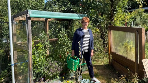 Gabriele Stähler steht neben einen Beet im Garten und hat eine Gießkanne in der Hand. 