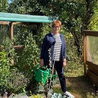 Gabriele Stähler steht neben einen Beet im Garten und hat eine Gießkanne in der Hand. 