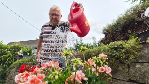 Ein Mann gießt Blumen in einem Garten.
