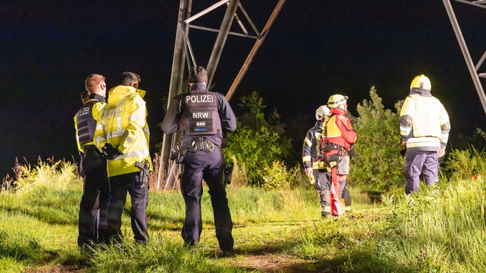 Einsatzkräfte der Polizei sowie Höhenrettung stehen auf einer begrünten Fläche und besprechen sich