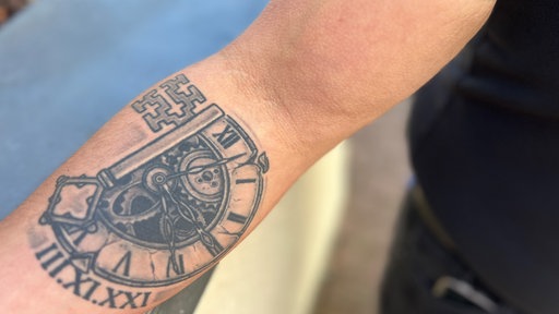 Ein Unterarm mit einem Tattoo. Das Tattoo zeigt einen Schlüssel und einen Kompass.