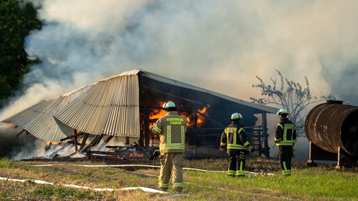 Eine brennende Scheune. Davor drei Feuerwehrmänner der Feuerwehr Lippetal.