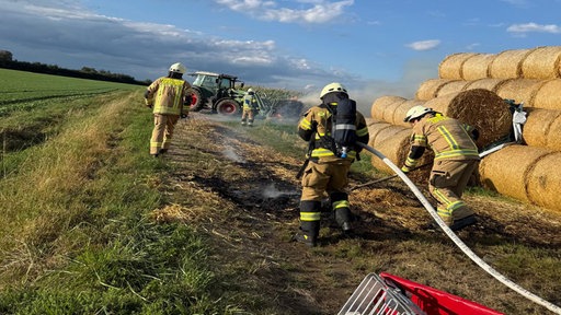 Feuerwehrmänner im Löscheinsatz auf einem Feld mit Heuballen.