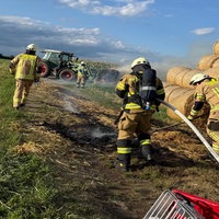 Feuerwehrmänner im Löscheinsatz auf einem Feld mit Heuballen.