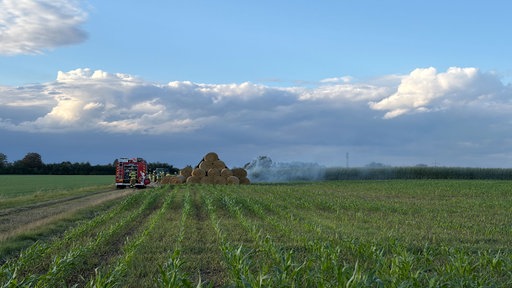 Qualmende Heuballen auf einem Feld. Daneben ein Feuerwehrfahrzeug.