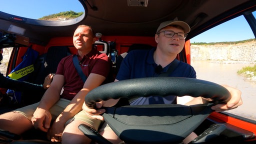 Zwei Männer sitzen in einem Fahrzeug.