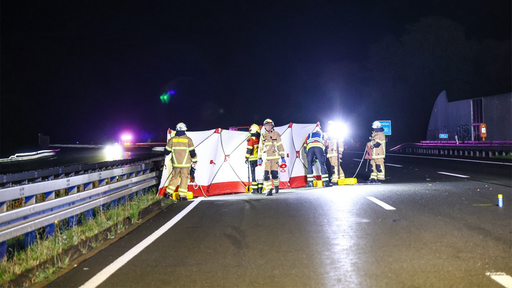 Auf der Fahrbahn der Autobah ist ein weiß-roter Sichtschutz aufgebaut. Davor sind mehrere Feuerwehrleute.