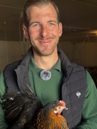 Ein Mann der lächelt und ein Huhn in den Armen hat