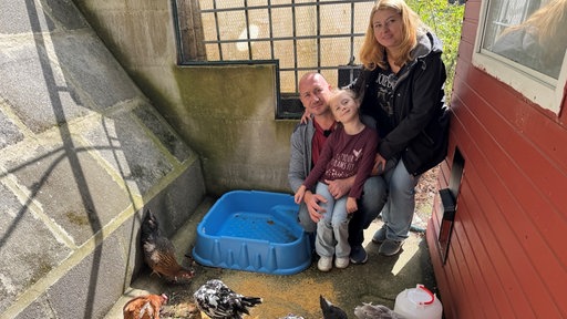 Eine dreiköpfige Familie in einem Stall mit Hühnern