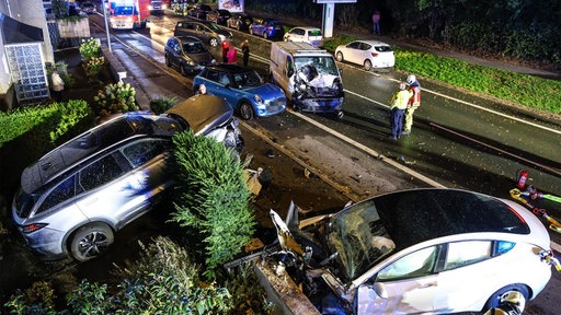 Mehrere zerstörte Fahrzeuge stehen auf einer Straße, Rettungskräfte stehen in der Nähe