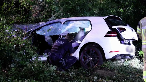 Ein Polizist schaut sich den völlig zerstörten weißen Unfallwagen an.