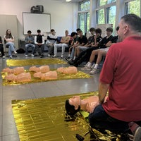 Ein Mitarbeiter des Deutschen Roten Kreuzes hockt beim Reanimationsunterricht vor den Schülern.