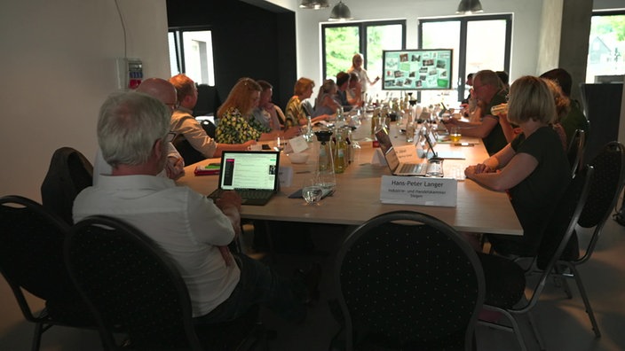 Menschen sitzen an einem Konferenztisch vor einem Bildschirm