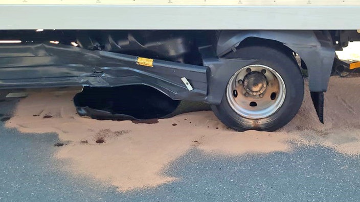 Ein aufgerissener Tank eines LKWs. Zudem ist unter dem beschädigten LKW bräunlicher Sand.