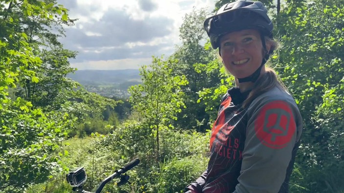 Martina Libera sitzt auf dem Mountainbike im Wald am Berg um den Danzturm in Iserlohn und lacht in die Kamera