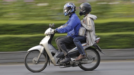 Zwei Personen fahren auf einem Motorroller