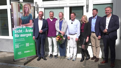 Menschen stehen neben einem Plakat und machen ein gemeinsames Foto