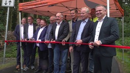 Männer schneiden ein rotes Band durch.