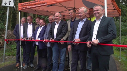 Männer schneiden ein rotes Band durch.