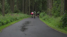 Drei Menschen fahren auf dem Fahrrad weg.