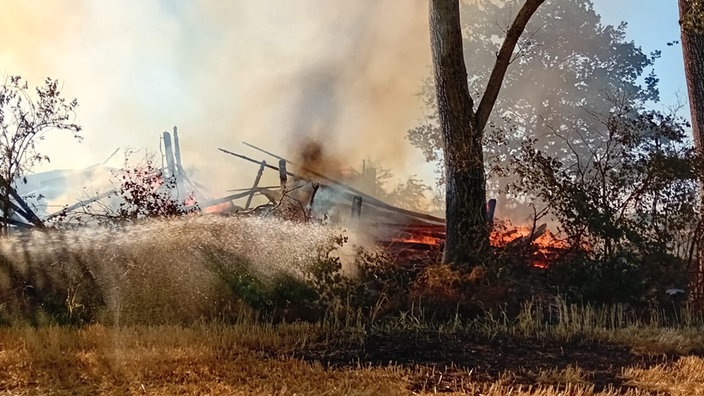 Eine Scheune steht in Flammen und ist in sich zusammengebrochen.
