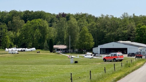 Auf einem Flugplatz stehen mehrere Segelflugzeuge und ein Einsatzwagen.