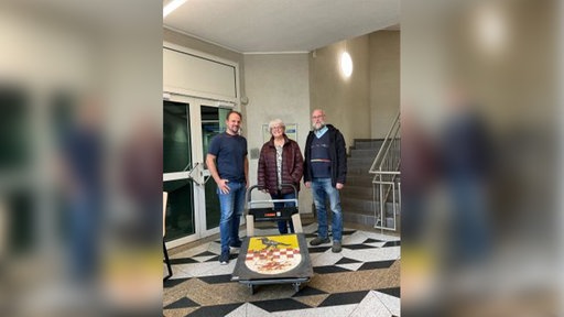 Drei Personen stehen neben dem Stadtwappen der Stadt Kierspe