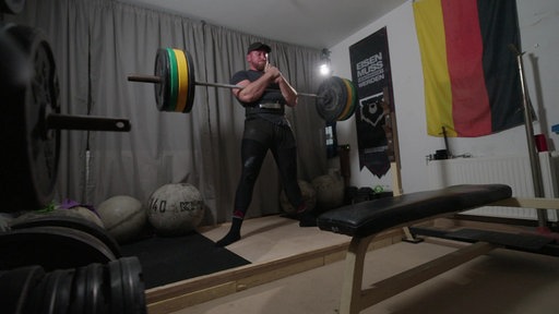 Ein Mann trainiert mit Gewichten in einem kleinen Trainingsraum