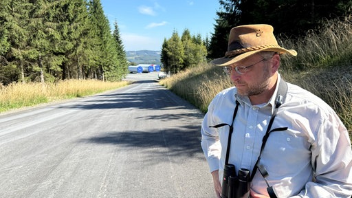 Ein Mann mit einem Fernglas steht auf einer Waldstraße