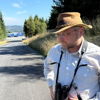 Ein Mann mit einem Fernglas steht auf einer Waldstraße
