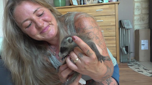 Eine Frau hält lächelnd ein Waschbärbaby in der Hand
