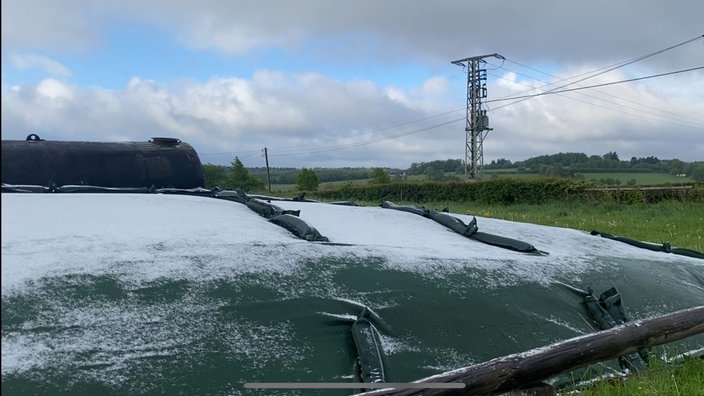 Leichter Schnee liegt auf einer grünen Plane in einem Feld