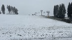 Eine dünne Schneedecke liegt über einem Hügel mit einem Lift