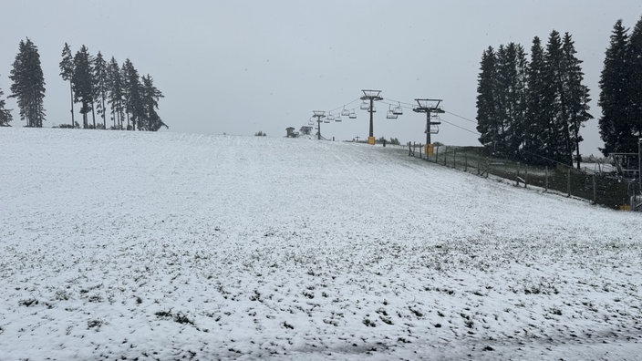 Eine dünne Schneedecke liegt über einem Hügel mit einem Lift