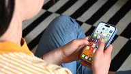 Eine Jugendliche sitzt auf dem Boden und hält ein Smartphone in der Hand