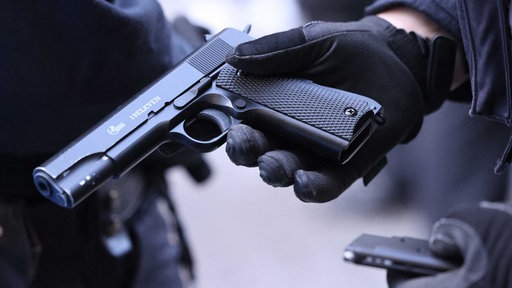 Eine Hand in einem schwarzen Handschuh hält eine schwarze Softairwaffe,