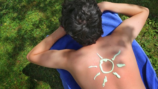 Eine Person trägt eine Sonne gemalt aus Sonnencreme auf dem Rücken