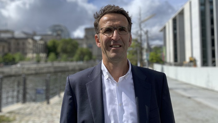 Mann mit Brille trägt Anzug und schaut lächelnd über Kamera hinweg