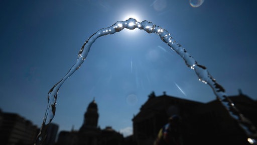 Die Wasserfontäne eines Trinkbrunnens vor blauem Himmel und strahlender Sonne