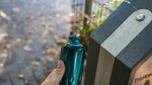Eine Flasche wird an einem Trinkwasserbrunnen aufgefüllt, man sieht nur die Hand. 