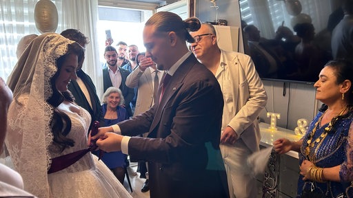 Ein Mann bindet vor der Hochzeit eine Schleife an der Vorderseite des Brautkleids