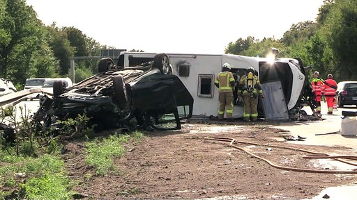 Mehrere Einsatzkräfte stehen um das auf der Seite liegende Wohnmobil und den auf dem Dach liegenden Pkw.