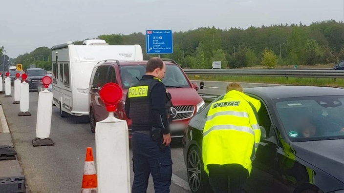 Polizisten stehen auf einer separaten Spur an der Autobahn und sprechen mit dem Fahrer eines Auto. Hinter ihm stauen sich weitere Fahrzeuge.